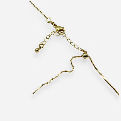 Detalle de collar con colgante irregular dorado y cristal central complementando un look elegante.