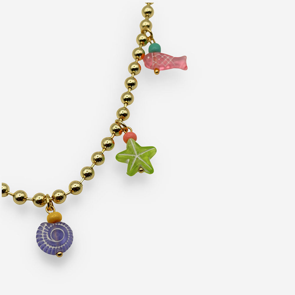 Detalle de collar con dijes de peces, estrella de mar y conchas que aporta un toque divertido y colorido al look.