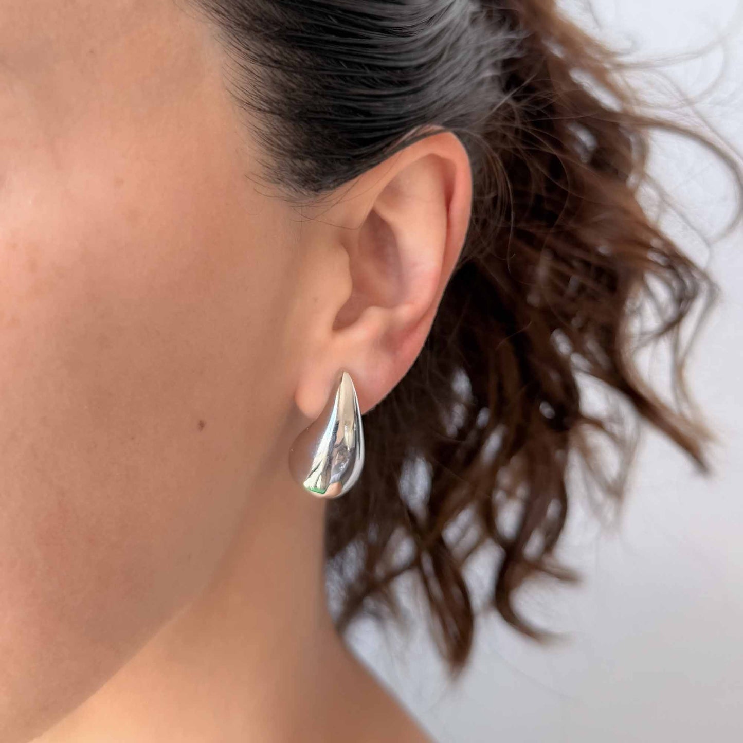 Mujer usando aretes plateados pequeños con diseño de gota brillante