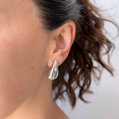 Mujer usando aretes plateados pequeños con diseño de gota brillante
