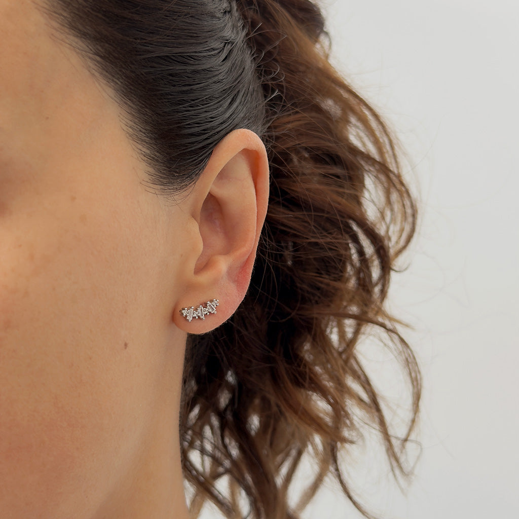 Mujer usando aretes tipo topo con circonias blancas en posición horizontal para crear un ear stack moderno.