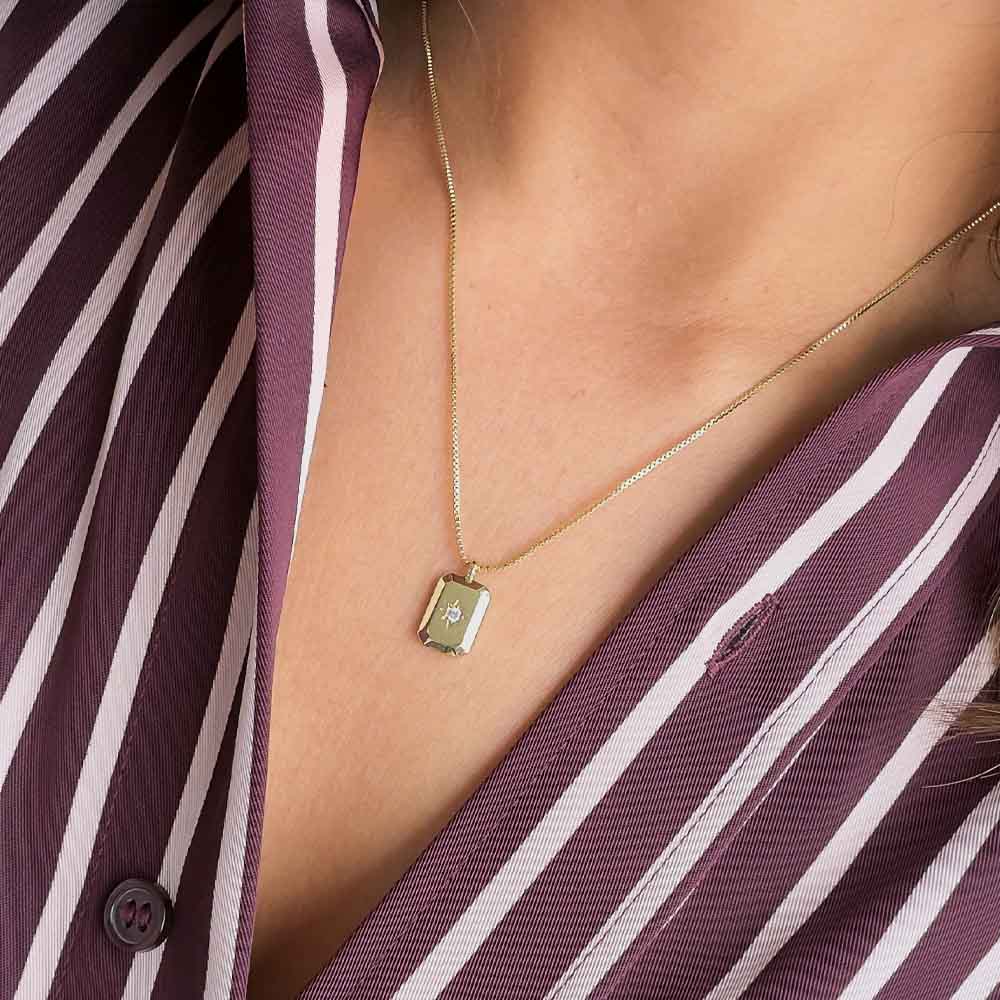 Mujer usando collar con dije rectangular y circonia central para mostrar su tamaño y caída sobre el escote.