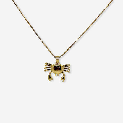 Collar dorado con dije de cangrejo sobre fondo neutro