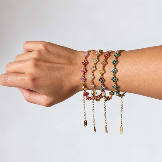muñeca de una mujer usando pulseras doradas en acero con forma de treboles y circonias de colores
