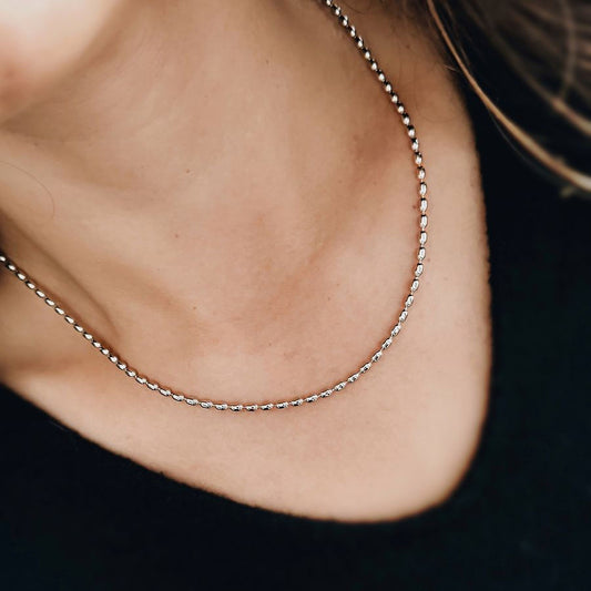 Cadena plateada delgada en bronce rodinado con estilo clásico y versátil sobre el cuello de una mujer que lleva un saco negro